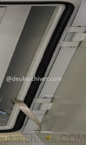 Close-up of a control panel door with a silver flexible braided copper bonding strap connected across the white painted hinge, and a yellow grounding symbol sticker on the panel frame for reliable electrical continuity and safety grounding.